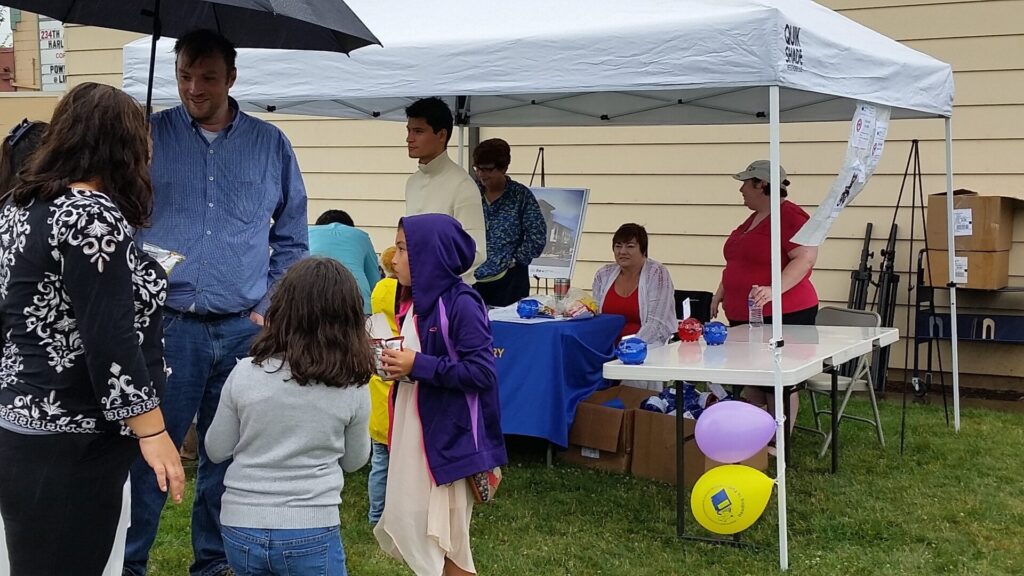 FreindsTent2015 Adults and children gather in front of a Library tent at an event, with food